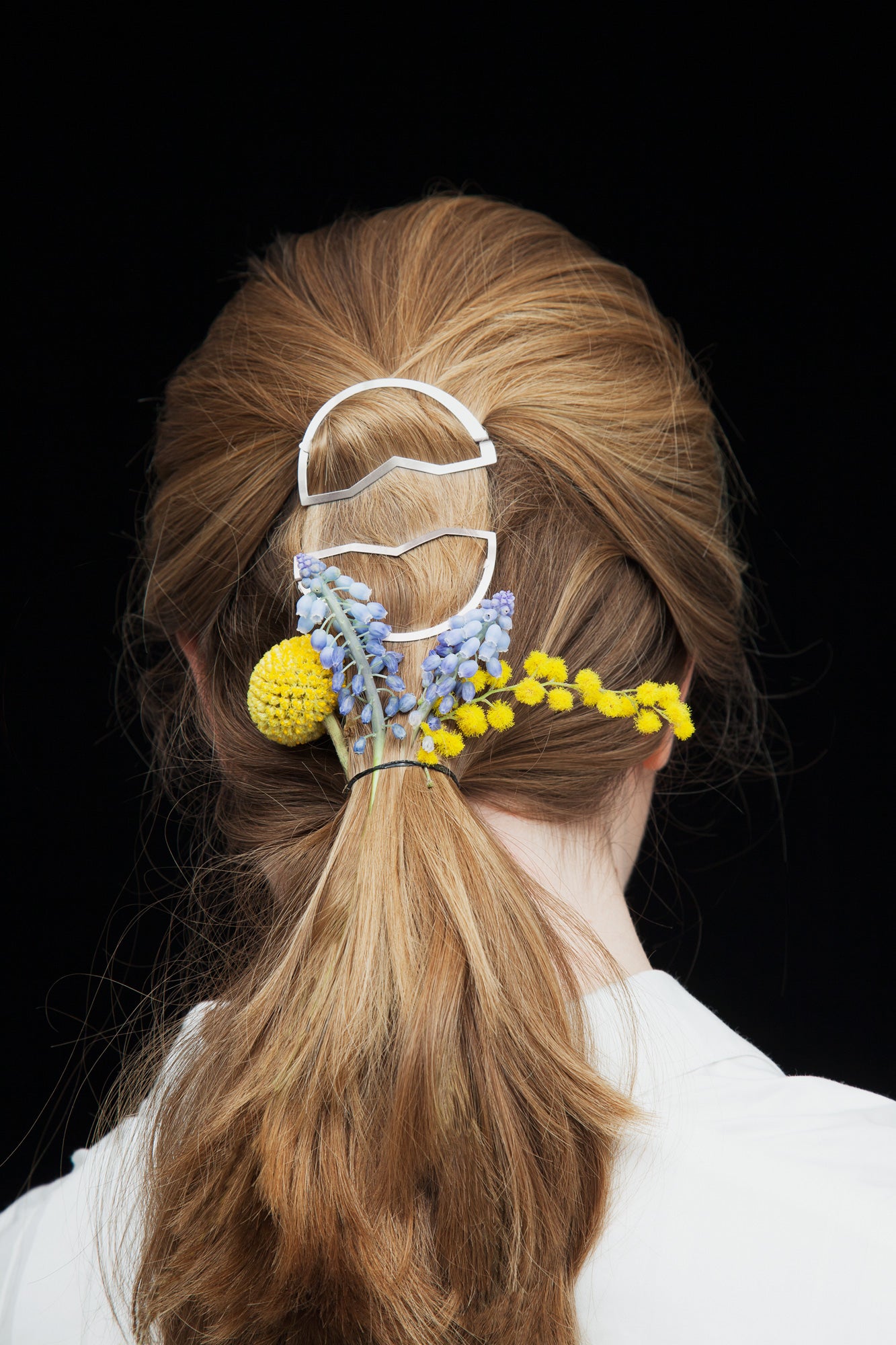 back view of model wearing a low ponytail accented with flowers and two designer hair clips CYNARA by CLINQ